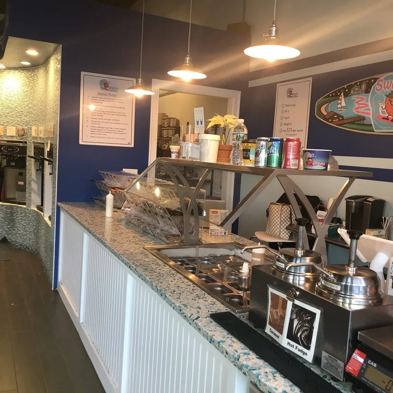 The Sweet Waves counter with a topping bar, hot fudge and caramel warmers, and a blue wall with a surfboard sign